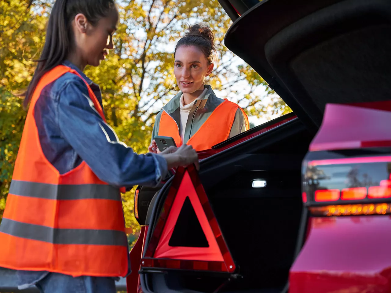 Two women with safety vests and a warning triangle next to a Volkswagen