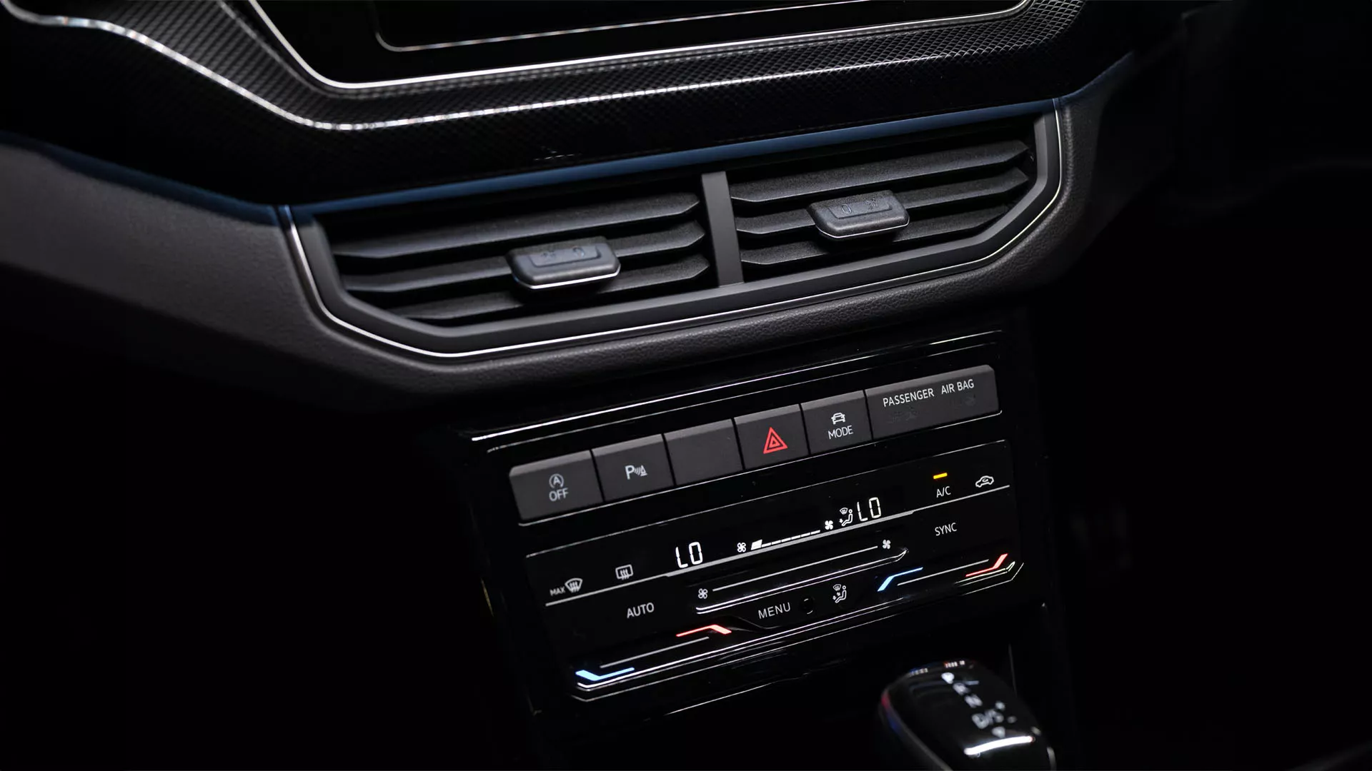 View of the centre console with screen, air conditioning and gear shift. A summer landscape is visible through the front windscreen.