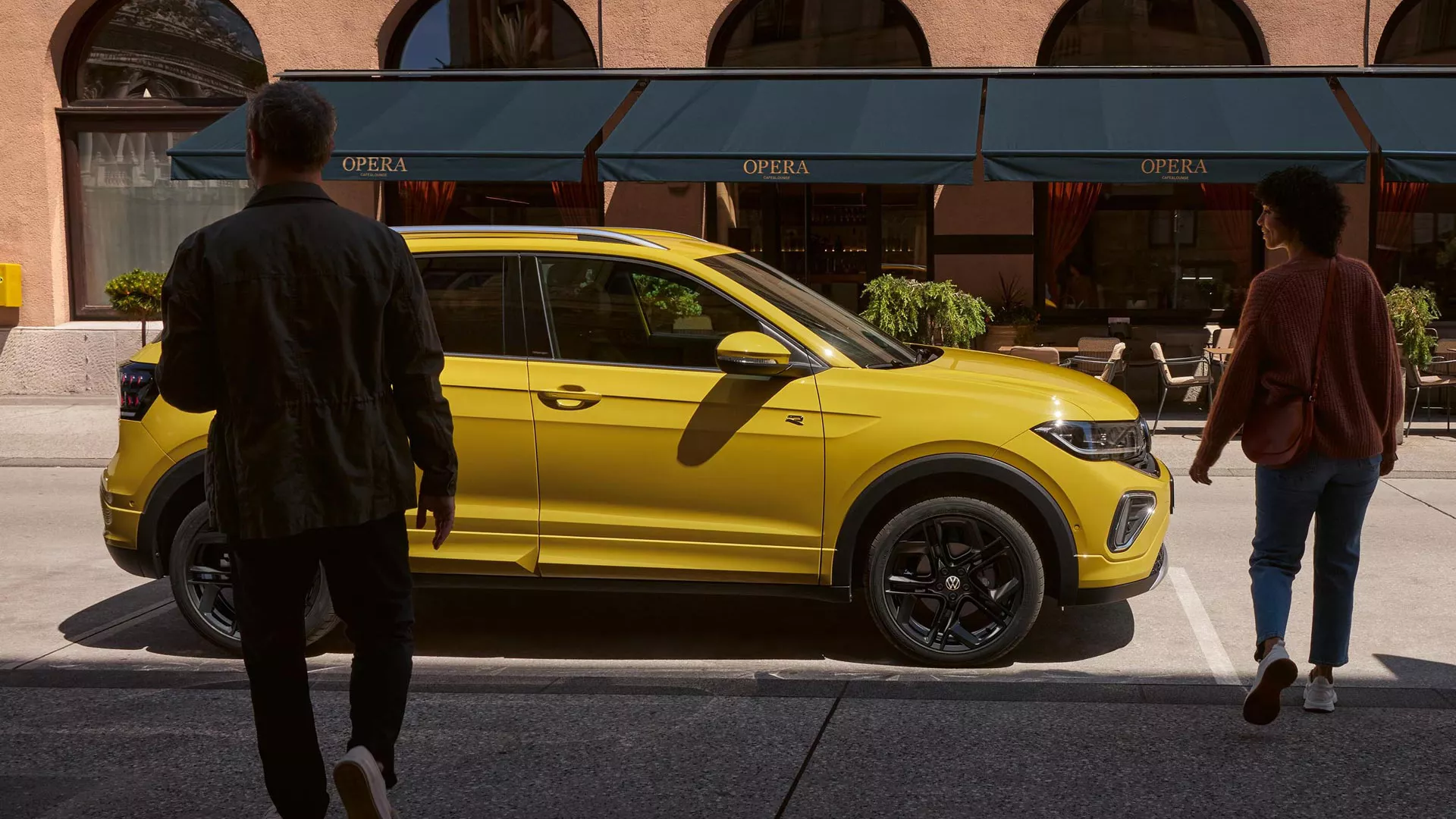 A man and woman approach a yellow VW T-Cross on the side of the road.