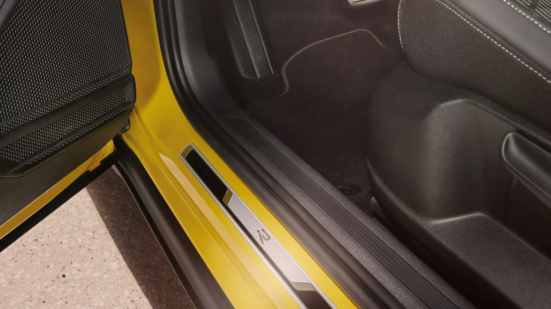 View of the lower part of the driver’s seat of the yellow VW T-Cross with the front door open with the brushed stainless steel door sill.