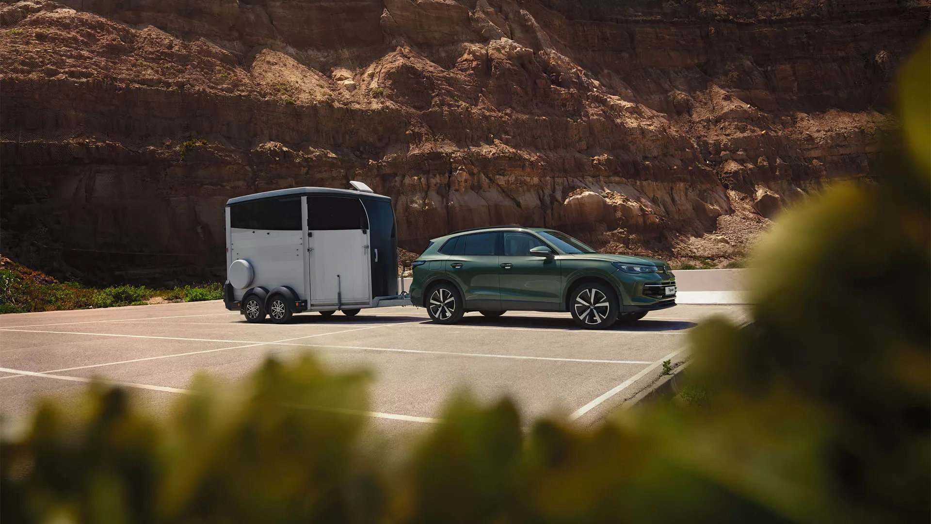 Dark green VW Tiguan with horse trailer parked in front of a rocky landscape.