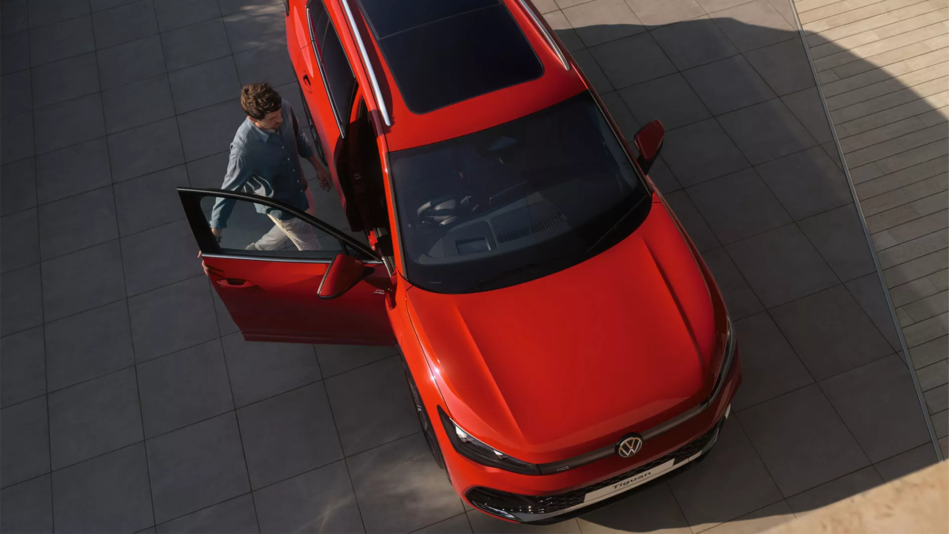 Top shot of the half open tilting and sliding panoramic sunroof on a red VW Tiguan. A young woman can be seen on the driver seat.