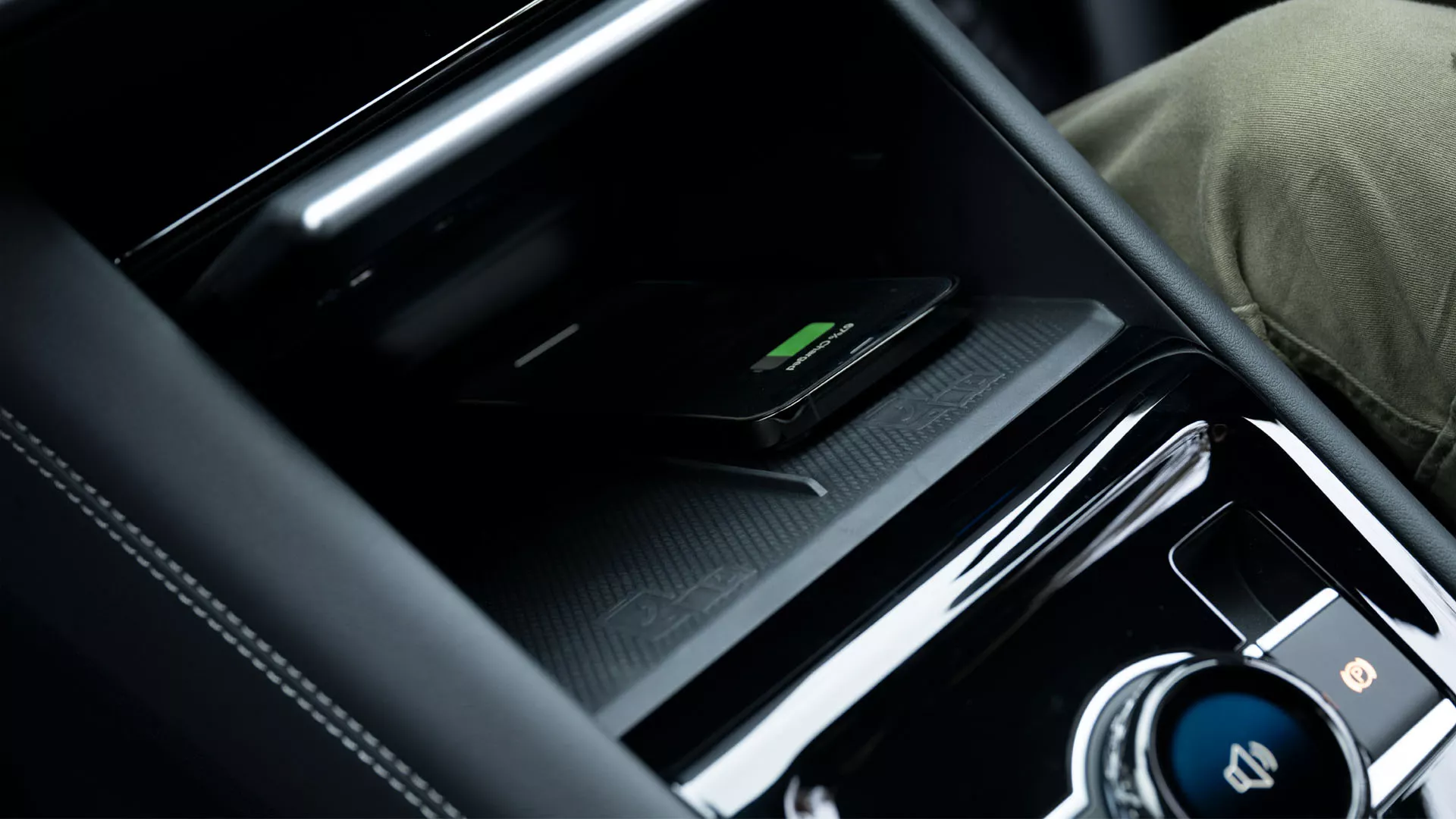 Detailed view of the interior of the VW Tiguan focusing on the centre console. One hand opens a storage compartment from the driver seat for wirelessly charging a mobile phone.