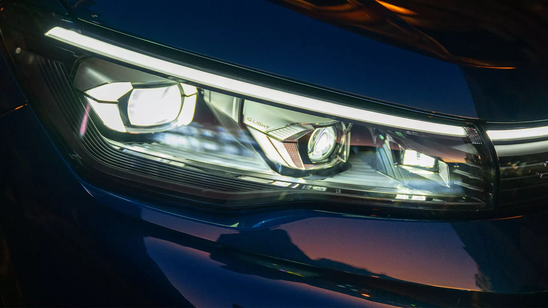 Detailed view of the front signature light of a red VW Tiguan in a car park.